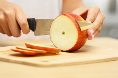 Woman cutting fresh apple at wooden table indoors, closeup