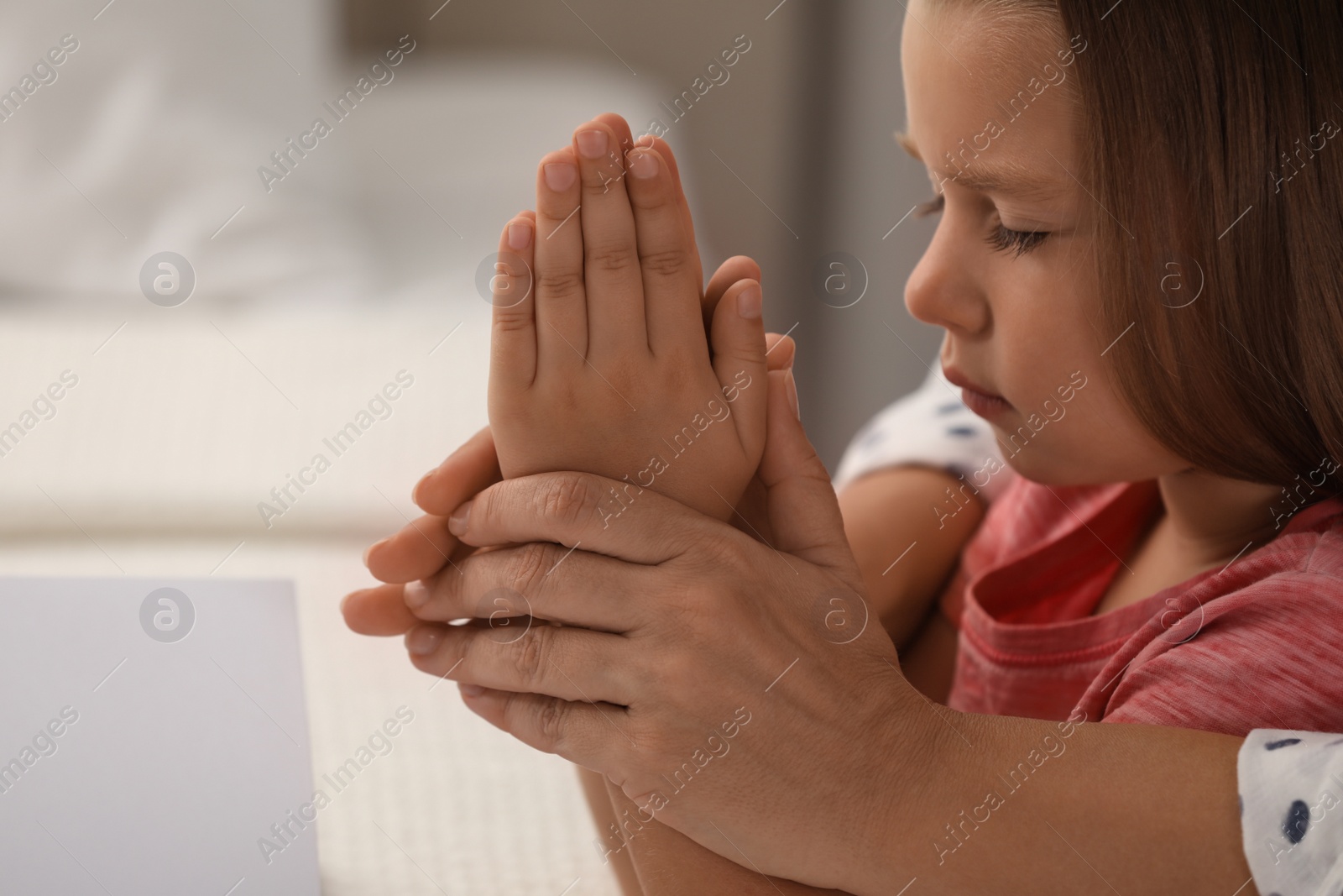 Photo of Mature woman with her little granddaughter praying together indoors, closeup