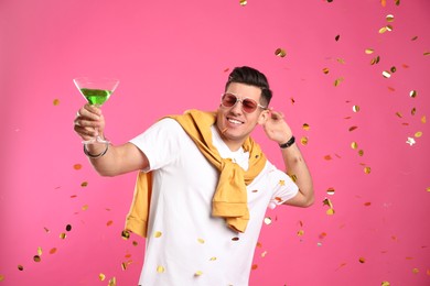 Happy man with cocktail and confetti on pink background