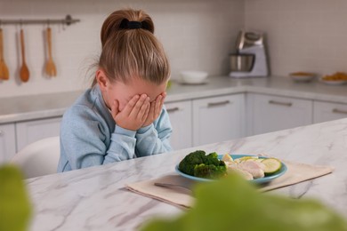 Photo of Cute little girl crying and refusing to eat dinner in kitchen