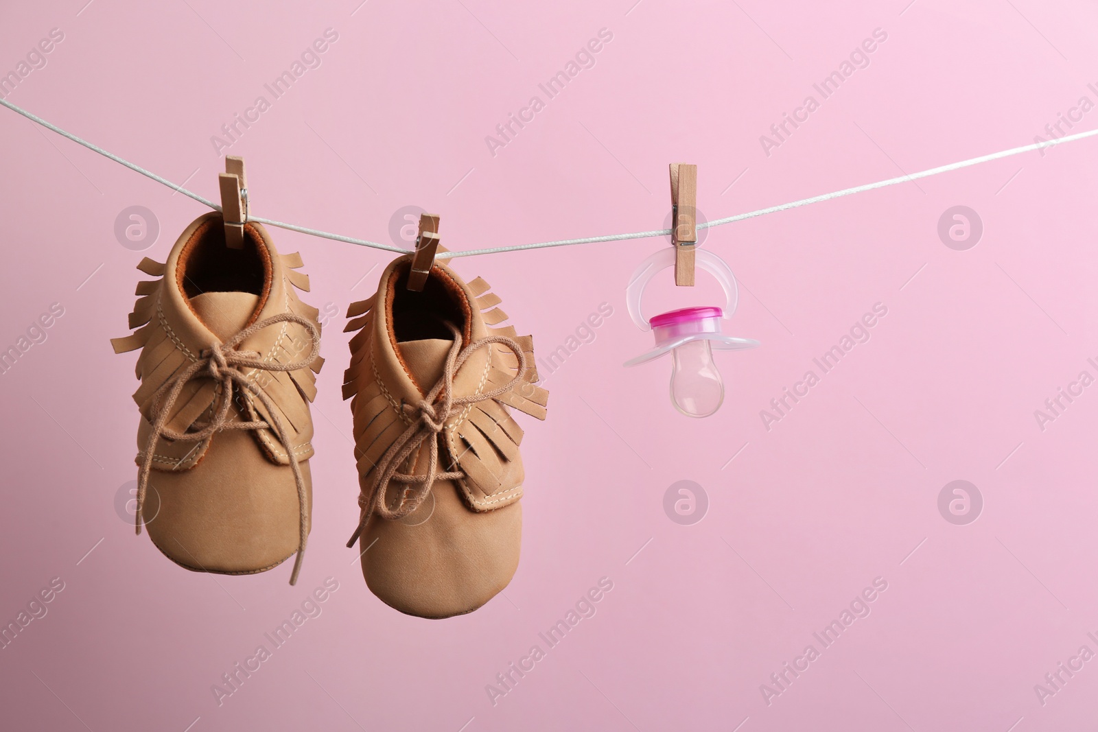 Photo of Small shoes and pacifier hanging on washing line against color background, space for text. Baby accessories