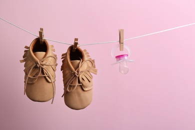 Photo of Small shoes and pacifier hanging on washing line against color background, space for text. Baby accessories