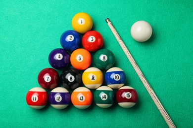 Photo of Set of billiard balls and cue on green table, flat lay
