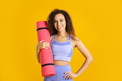 Beautiful African American woman with yoga mat on yellow background