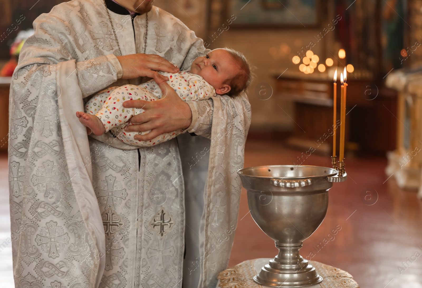 Photo of MYKOLAIV, UKRAINE - FEBRUARY 27, 2021: Priest holding baby in Kasperovskaya icon of Mother of God cathedral during baptism ceremony, closeup