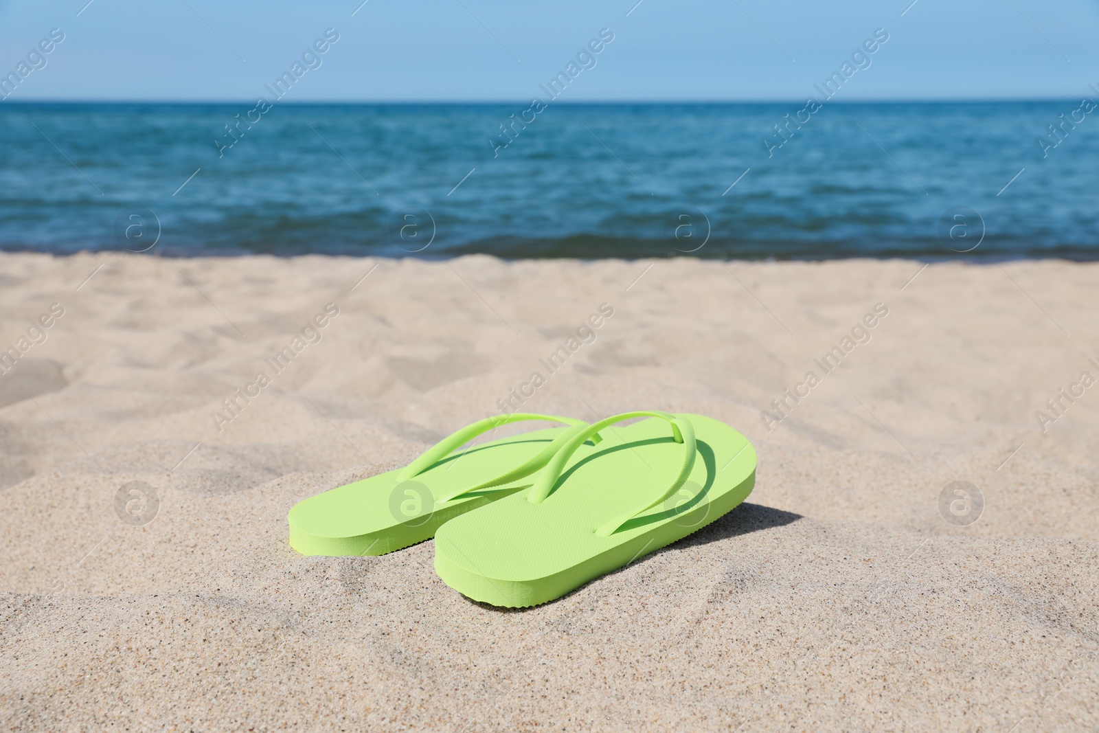 Photo of Stylish light green flip flops on beach sand, space for text