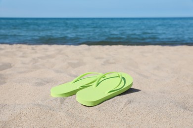 Stylish light green flip flops on beach sand, space for text