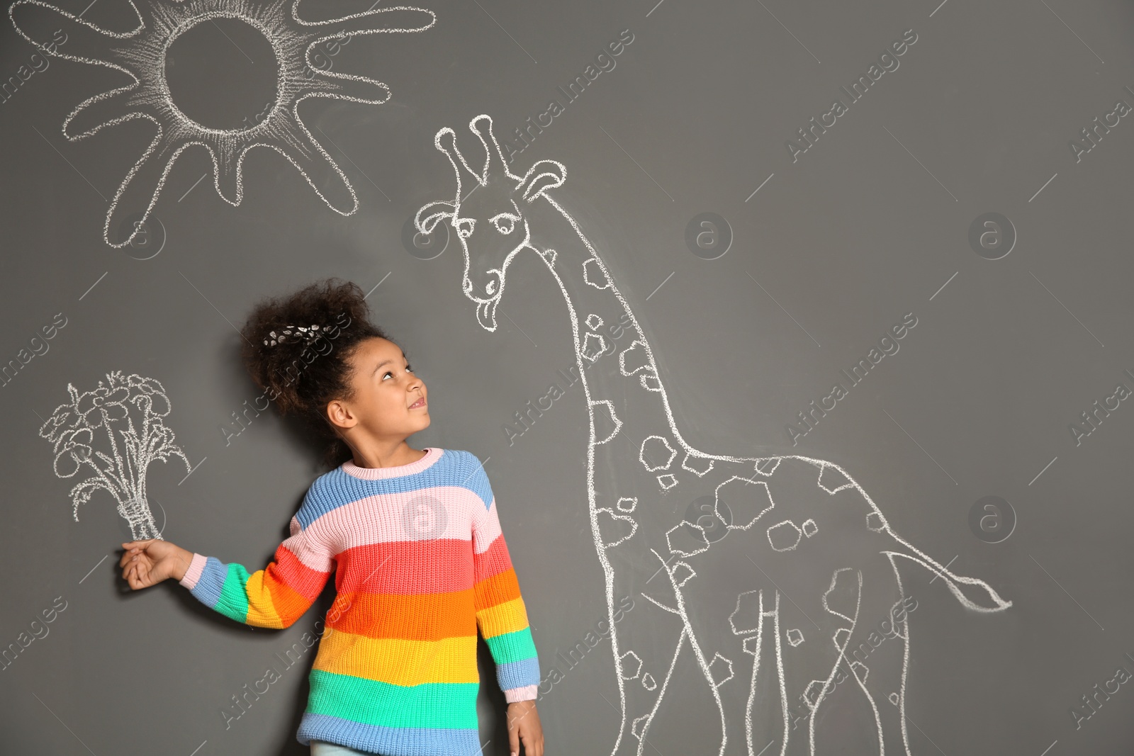 Photo of African-American child playing with chalk drawing of giraffe and flowers on grey background