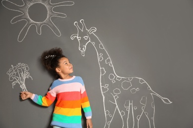 African-American child playing with chalk drawing of giraffe and flowers on grey background