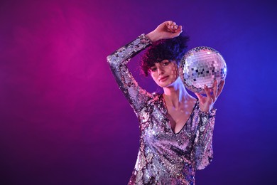 Beautiful young woman with disco ball posing on color background in neon lights. Space for text