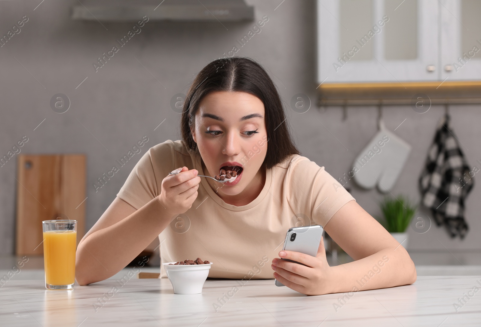 Photo of Woman using smartphone while having breakfast at table in kitchen. Internet addiction