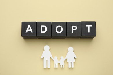 Photo of Family figure and word Adopt made of cubes on beige background, flat lay