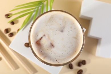 Photo of Refreshing iced coffee with milk in glass and beans on pale yellow table, top view