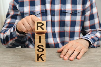 Photo of Man destroying tower of cubes with word Risk at table, closeup