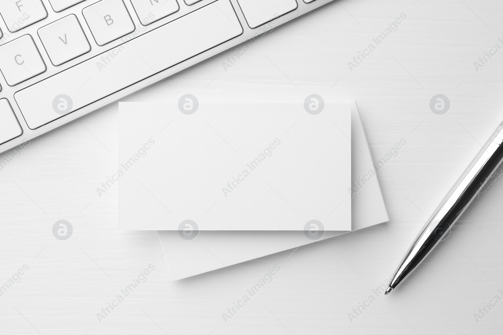 Photo of Blank business cards, keyboard and pen on white table, flat lay. Mockup for design