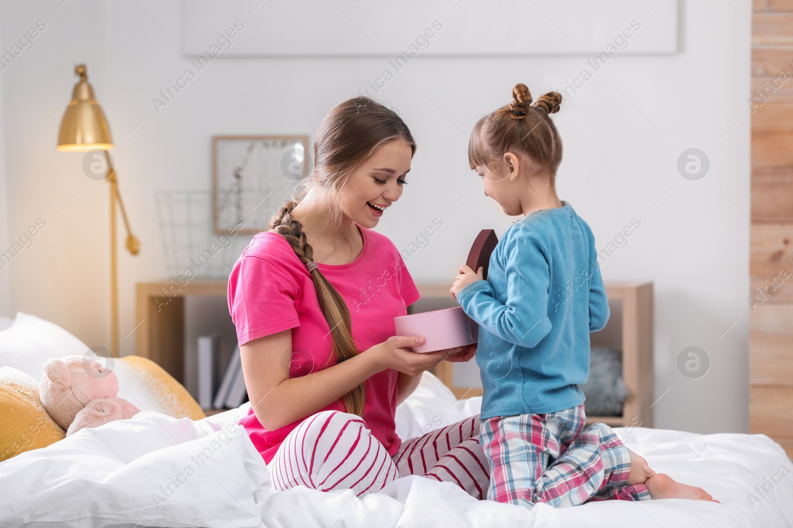 Photo of Happy mother and daughter with gift on bed at home. International Women's Day