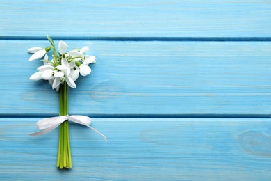 Beautiful bouquet of snowdrops on light blue wooden table, top view. Space for text