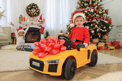 Cute little boy driving toy car in room decorated for Christmas