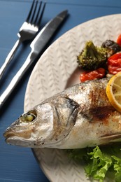 Photo of Delicious baked fish and vegetables served on blue table, closeup