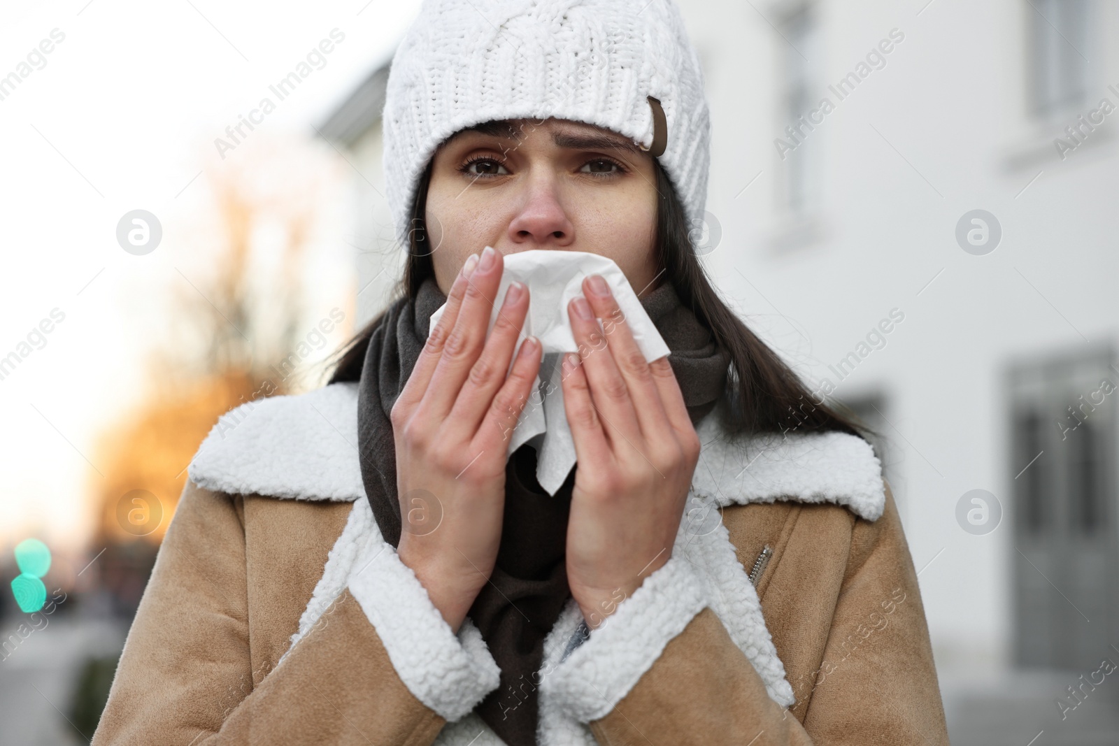 Photo of Woman with tissue blowing runny nose outdoors. Cold symptom