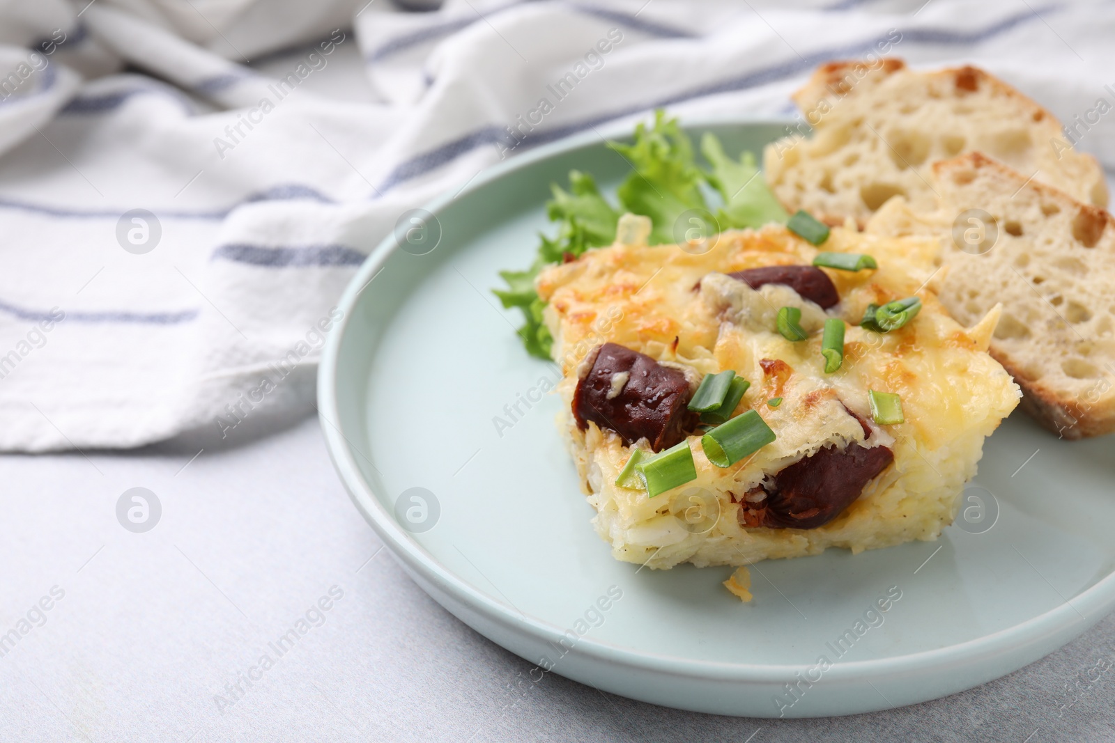 Photo of Tasty sausage casserole with green onion and bread on light grey table