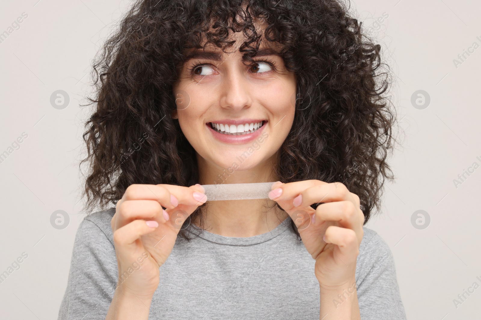 Photo of Young woman holding teeth whitening strip on light grey background