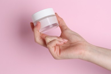 Woman holding jar of cream on pink background, closeup