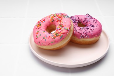 Glazed donuts decorated with sprinkles on white tiled table, closeup. Space for text. Tasty confectionery