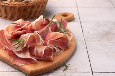Slices of tasty cured ham and rosemary on tiled table, closeup. Space for text