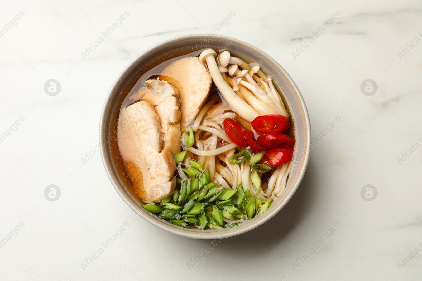 Photo of Delicious ramen with meat and mushrooms in bowl on white marble table, top view. Noodle soup