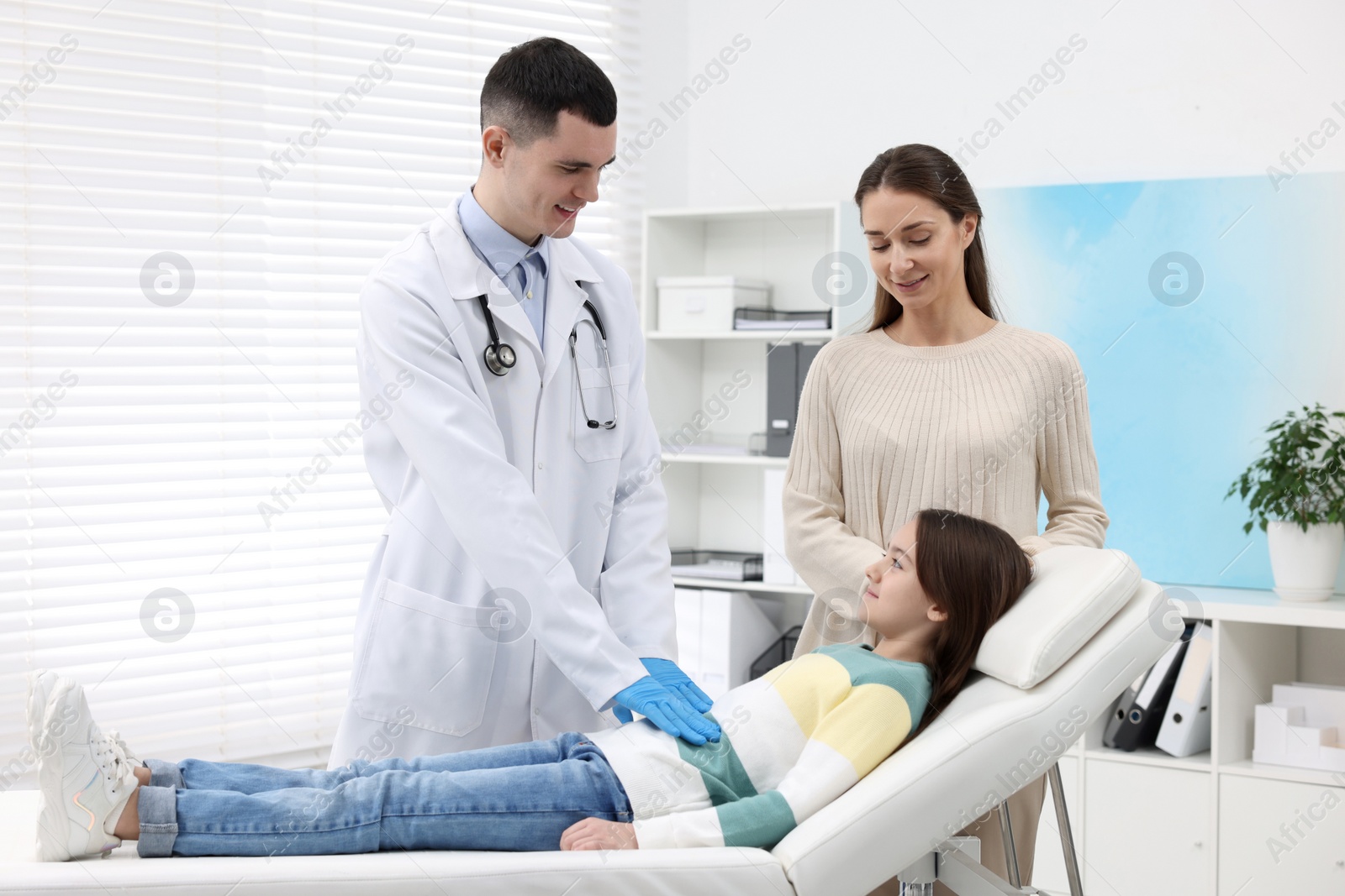 Photo of Gastroenterologist examining girl with stomach ache on couch in clinic