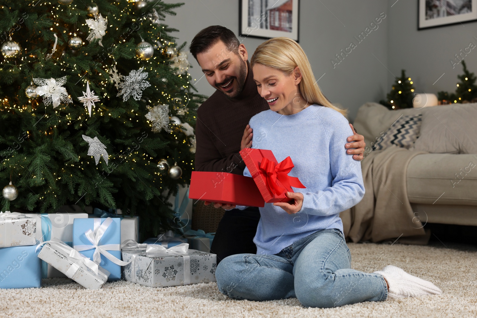 Photo of Happy man surprising his woman with Christmas gift at home