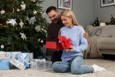 Happy man surprising his woman with Christmas gift at home