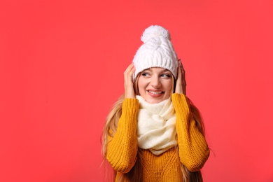 Portrait of emotional young woman in stylish hat, sweater and scarf on color background. Winter atmosphere