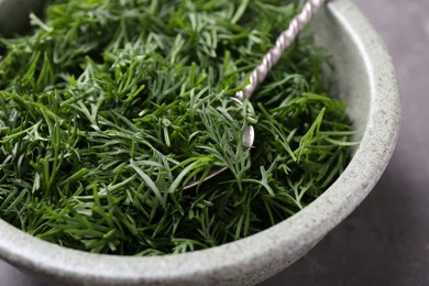 Photo of Fresh cut dill and spoon in bowl on table, closeup