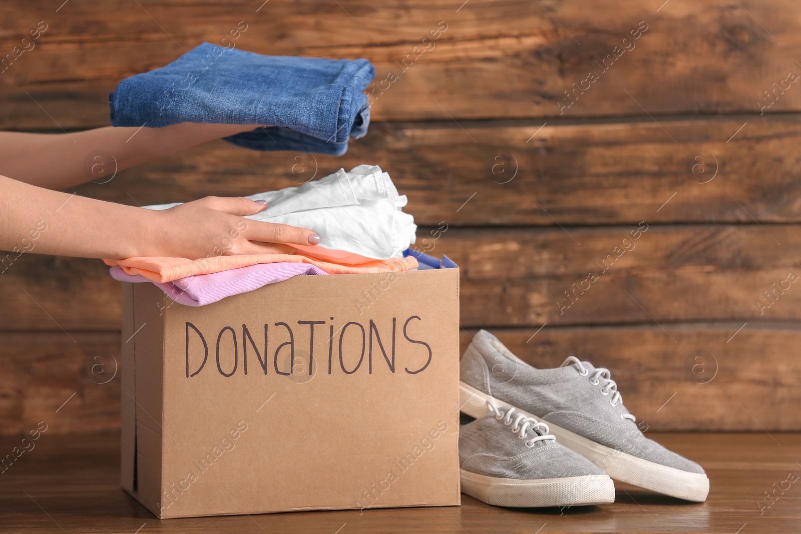 Photo of Female volunteer putting clothes into donation box on wooden background