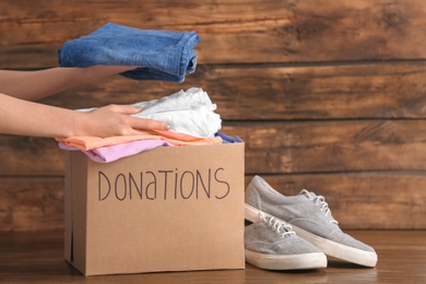 Female volunteer putting clothes into donation box on wooden background