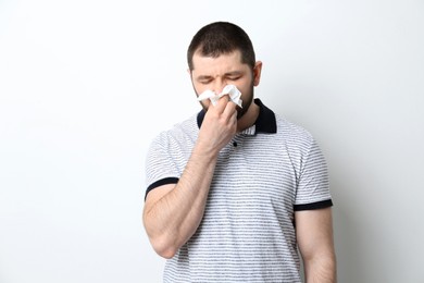 Man with tissue suffering from runny nose on white background