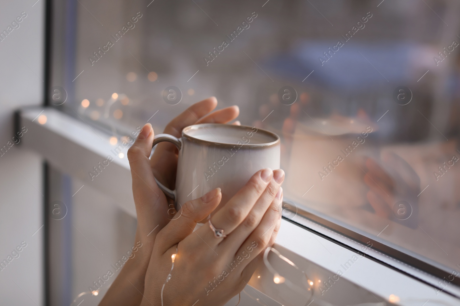 Photo of Young woman with cup of hot coffee near window, closeup