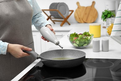 Woman pouring cooking oil from bottle into frying pan in kitchen, closeup