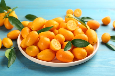 Photo of Fresh ripe kumquats in plate on light blue wooden table