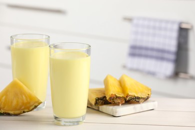 Photo of Glasses of tasty pineapple smoothie and cut fruit on white table indoors, space for text
