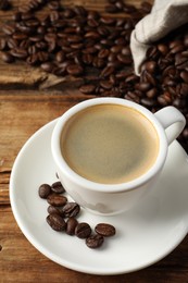 Cup of hot aromatic coffee and roasted beans on wooden table