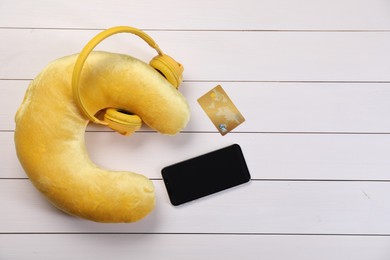 Photo of Yellow travel pillow with headphones, smartphone and credit card on white wooden background, flat lay. Space for text