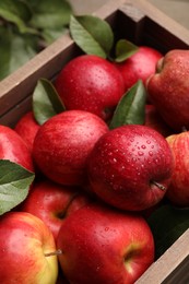 Photo of Crate with wet red apples and green leaves on table, closeup