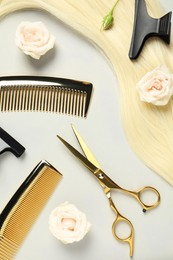 Flat lay composition with professional hairdresser tools, flowers and blonde hair strand on light grey background