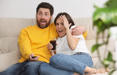Photo of Frightened couple watching TV on sofa at home