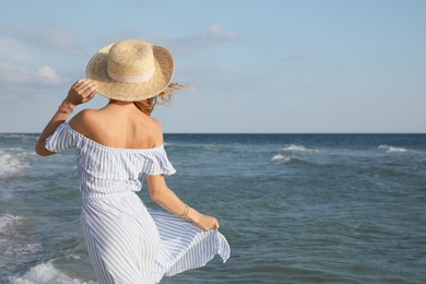 Photo of Woman with straw hat near sea on sunny day, back view