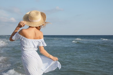 Woman with straw hat near sea on sunny day, back view