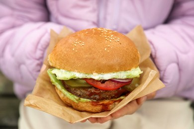 Photo of Little girl holding fresh delicious burger, closeup. Street food